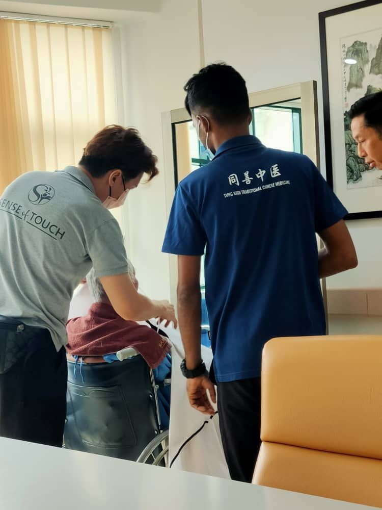 Two healthcare workers assisting a person in a wheelchair in an office setting.